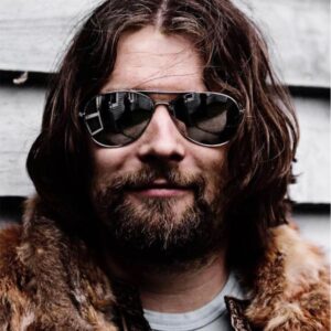 A headshot of Claus Raasted, keynote speaker at Evolve, wearing aviator sunglasses